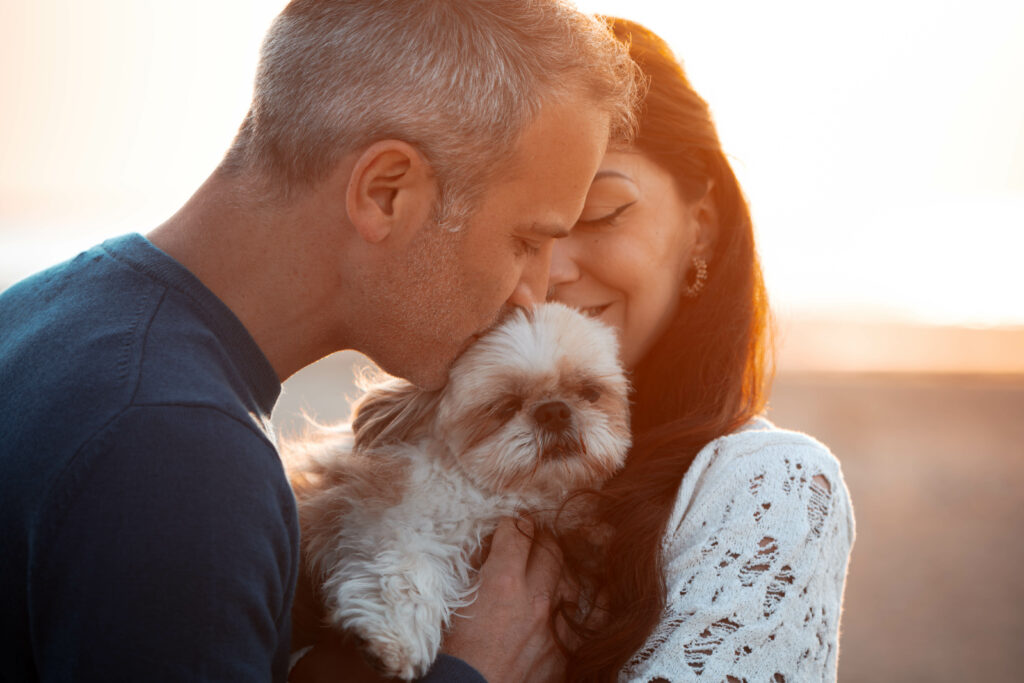 Un couple avec leur chien Patton, un Shih tzu, qu'ils tiennent dans leur bras et qu'ils embrassent sur une plage de normandie, à merville-franceville durant le coucher de soleil et la golden hour.