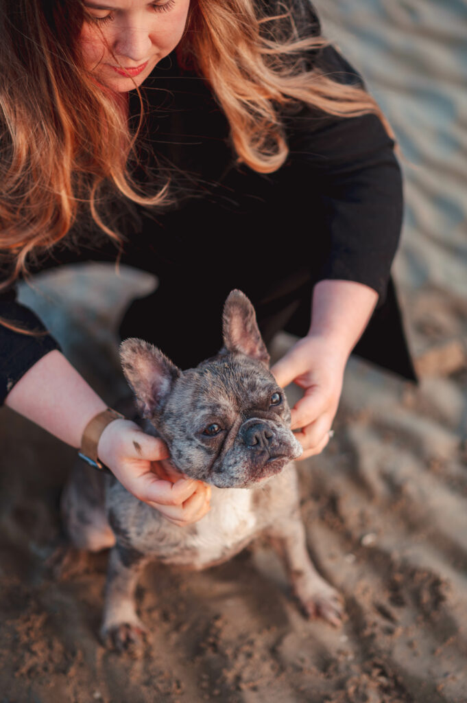 Femme avec son chien, un bouledogue français, sur une plage de Normandie à Merville Franceville près de Caen lors d'un lever de soleil pendant une golden hour. Portrait d'une famille avec son chien.